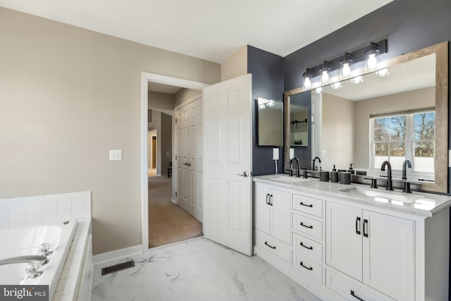 full bath with double vanity, marble finish floor, a relaxing tiled tub, and a sink