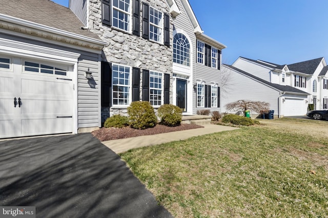 exterior space featuring stone siding, driveway, a front lawn, and a garage