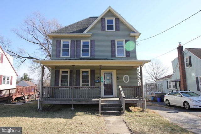 view of front of house featuring roof with shingles, a porch, and a front yard