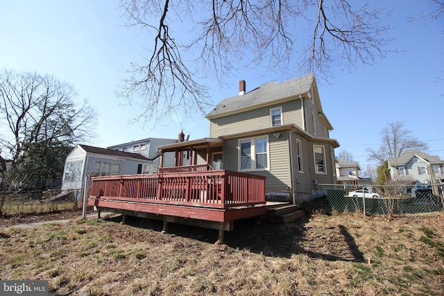 back of house featuring a wooden deck, a chimney, and fence