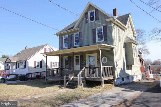 view of front facade featuring covered porch, a chimney, and roof with shingles