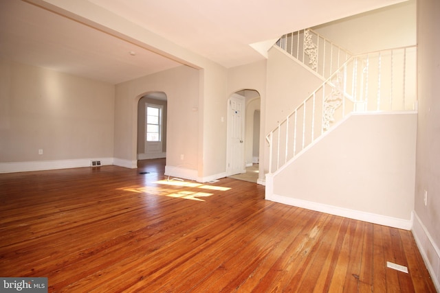 interior space with hardwood / wood-style floors, stairway, arched walkways, and baseboards