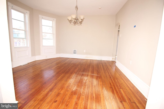 spare room featuring visible vents, light wood-style flooring, arched walkways, baseboards, and a chandelier