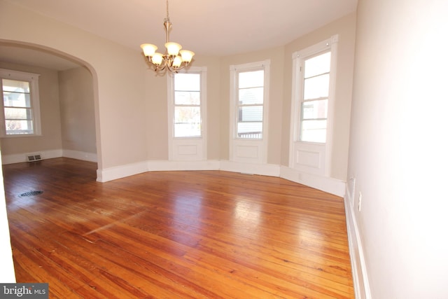 empty room featuring hardwood / wood-style floors, visible vents, baseboards, arched walkways, and a chandelier