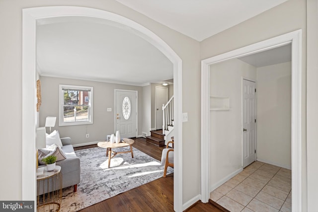 entryway featuring stairway, arched walkways, baseboards, and wood finished floors