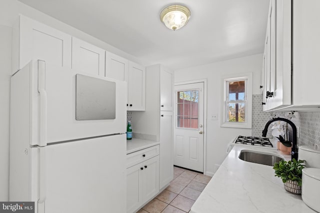 kitchen with light tile patterned floors, freestanding refrigerator, a sink, white cabinetry, and backsplash