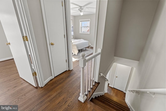 stairway featuring baseboards, wood finished floors, and a ceiling fan