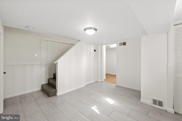 finished basement featuring stairs, a decorative wall, and visible vents