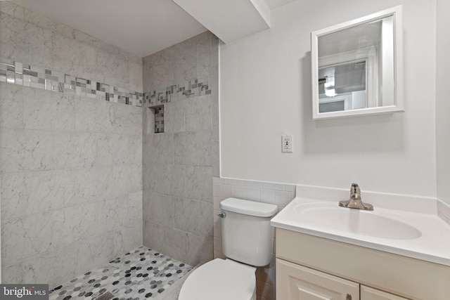 bathroom with a tile shower, toilet, vanity, and tile walls