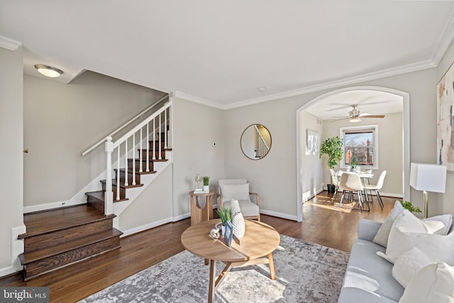 living room featuring ornamental molding, wood finished floors, stairway, arched walkways, and baseboards