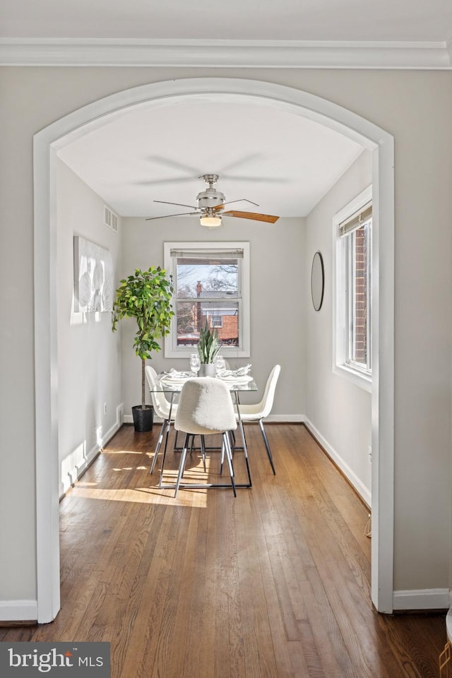 dining area featuring hardwood / wood-style floors, visible vents, arched walkways, and baseboards