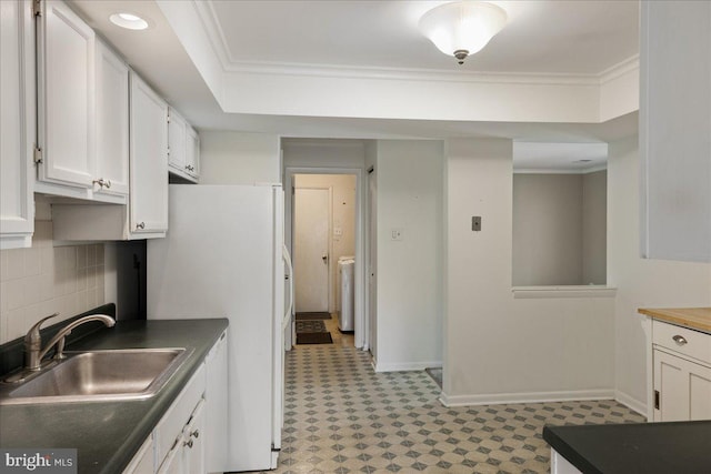 kitchen with dark countertops, crown molding, white cabinets, washer / clothes dryer, and a sink