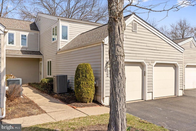 view of side of property with driveway, central AC, a garage, and a shingled roof