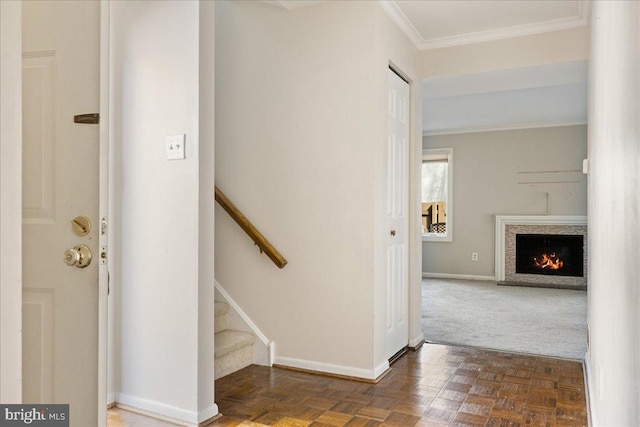 stairs with crown molding, baseboards, and a warm lit fireplace