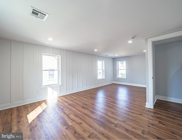 spare room with visible vents, recessed lighting, a decorative wall, baseboards, and dark wood-style flooring