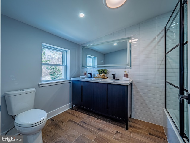 bathroom featuring wood tiled floor, toilet, double vanity, a tile shower, and a sink