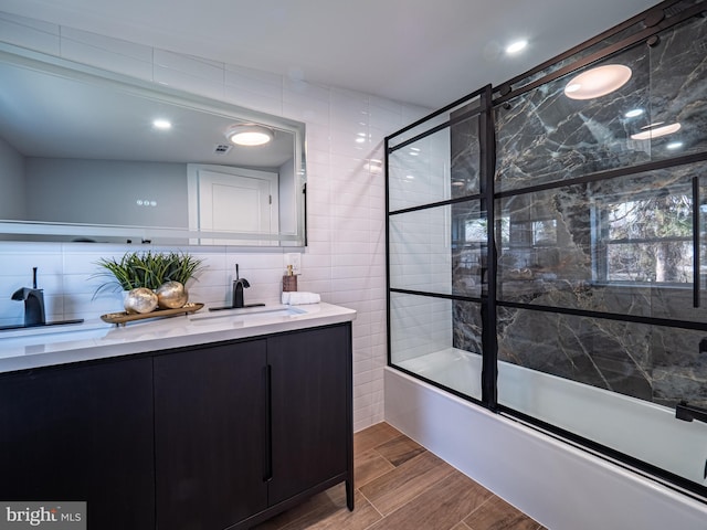 full bath with tile walls, vanity, wood tiled floor, and shower / bath combination with glass door