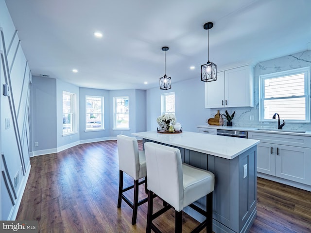 kitchen featuring a breakfast bar, dark wood-style flooring, a sink, white cabinetry, and a center island