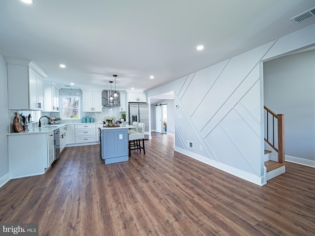 kitchen with visible vents, white cabinets, appliances with stainless steel finishes, a kitchen breakfast bar, and wall chimney exhaust hood