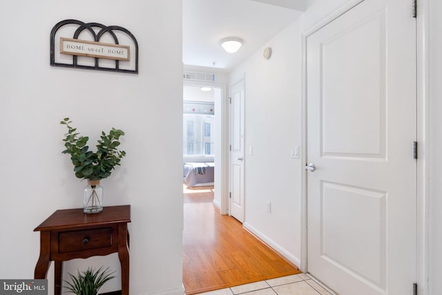 hallway featuring light tile patterned floors, baseboards, and visible vents