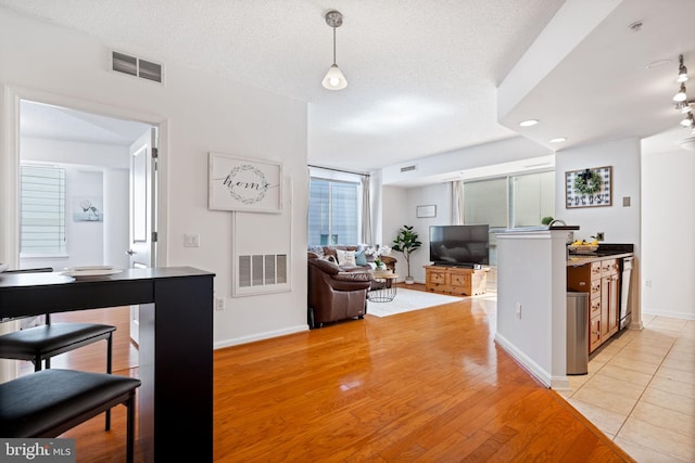 interior space featuring visible vents, light wood-style flooring, a textured ceiling, and baseboards