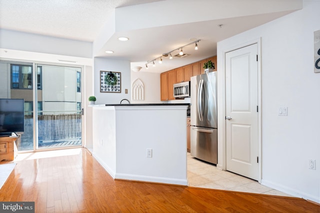 kitchen featuring a peninsula, light wood-style flooring, appliances with stainless steel finishes, dark countertops, and brown cabinets