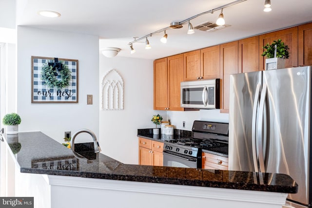 kitchen featuring visible vents, dark stone counters, appliances with stainless steel finishes, a peninsula, and brown cabinetry