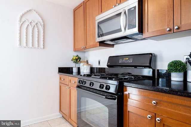 kitchen with brown cabinets, dark stone countertops, stainless steel microwave, black gas range oven, and baseboards