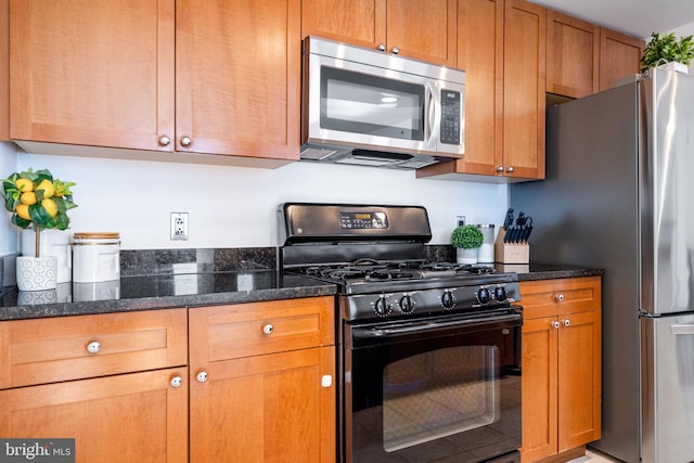 kitchen featuring brown cabinetry, appliances with stainless steel finishes, and dark stone counters