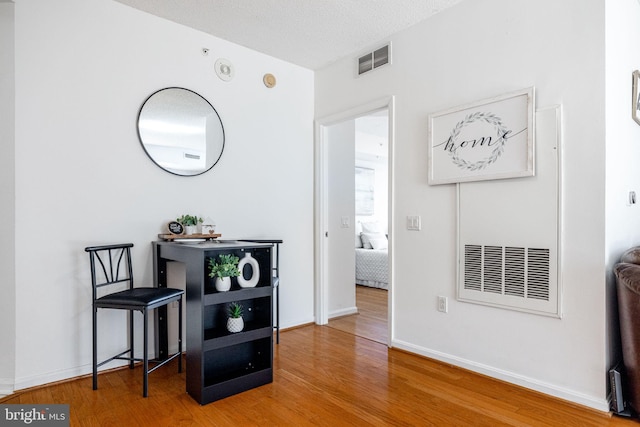 hall with a textured ceiling, wood finished floors, visible vents, and baseboards