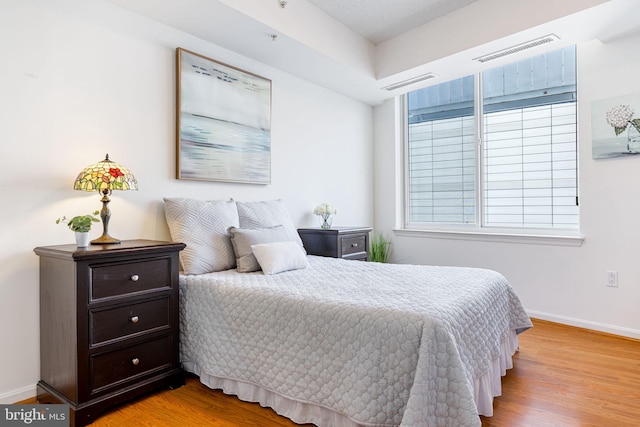 bedroom with wood finished floors, visible vents, and baseboards