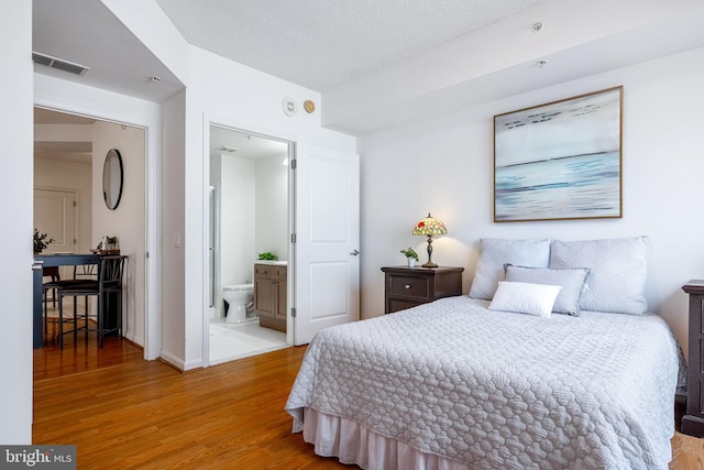 bedroom with visible vents, ensuite bathroom, a textured ceiling, wood finished floors, and baseboards