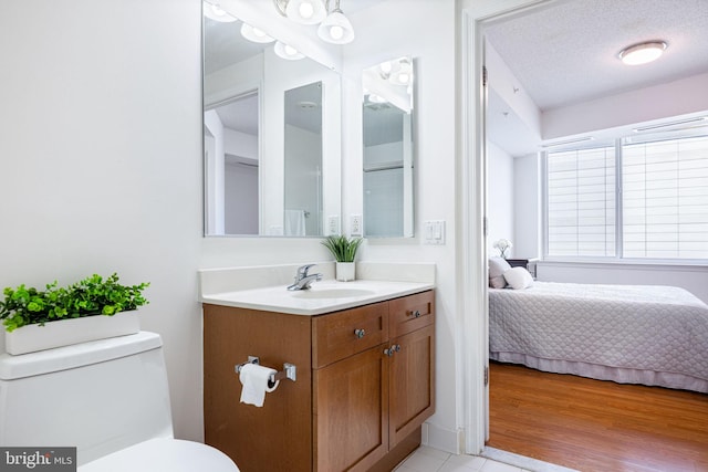 bathroom with toilet, vanity, ensuite bathroom, wood finished floors, and a textured ceiling