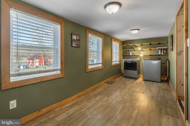 clothes washing area featuring laundry area, washer and dryer, light wood-style flooring, and baseboards