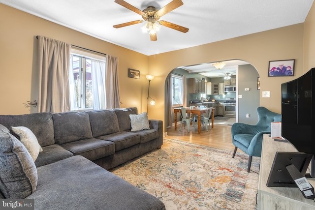 living room with ceiling fan, arched walkways, plenty of natural light, and light wood-style flooring