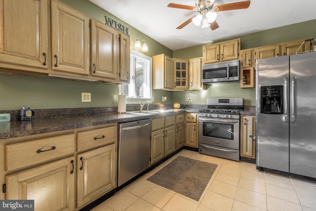 kitchen featuring a ceiling fan, a sink, dark countertops, appliances with stainless steel finishes, and light tile patterned floors