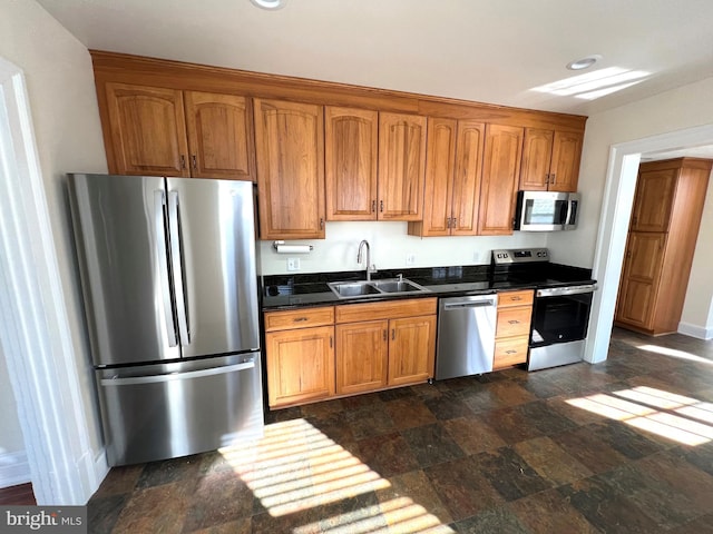 kitchen with a sink, stainless steel appliances, stone finish flooring, dark countertops, and brown cabinets