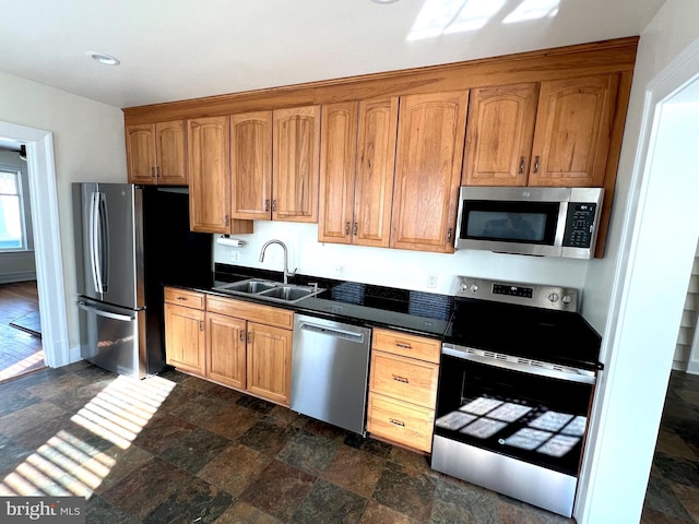 kitchen featuring dark countertops, stone finish flooring, baseboards, appliances with stainless steel finishes, and a sink