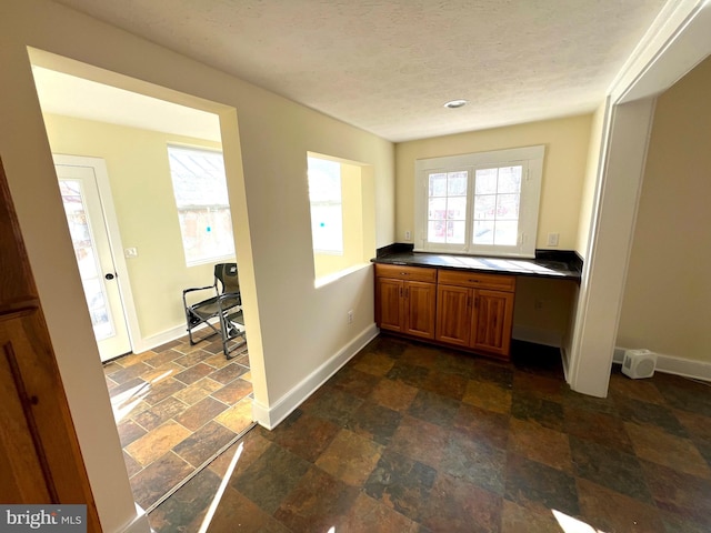 office featuring built in study area, a textured ceiling, stone finish flooring, and baseboards