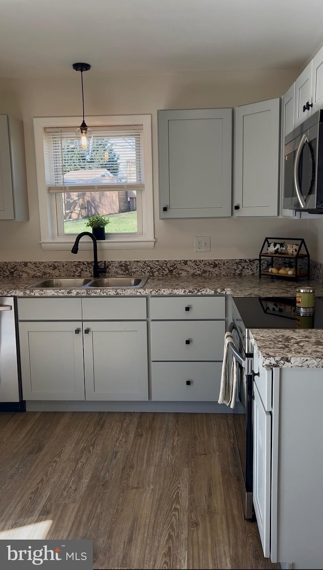 kitchen featuring a sink, decorative light fixtures, dark wood-style floors, stainless steel appliances, and light stone countertops