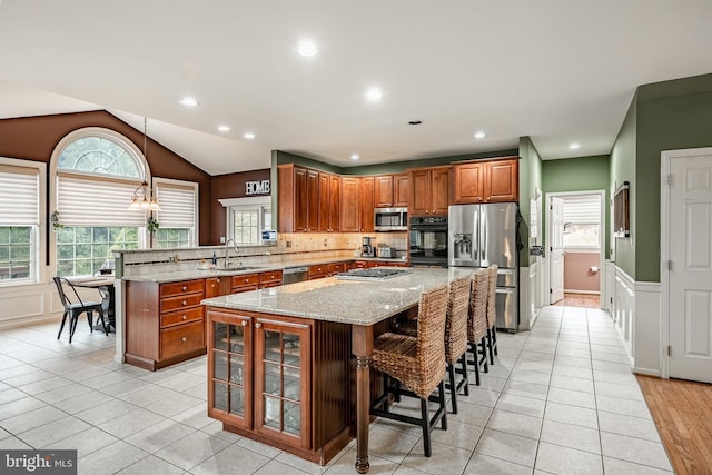 kitchen featuring light stone countertops, brown cabinetry, a peninsula, a sink, and appliances with stainless steel finishes