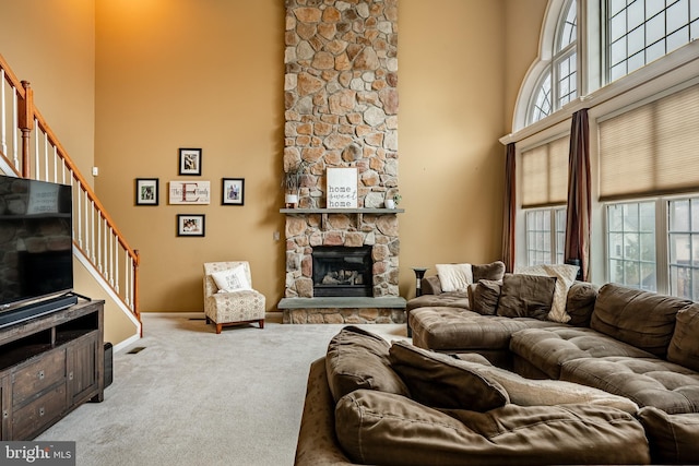 living room featuring carpet flooring, a healthy amount of sunlight, a stone fireplace, and a high ceiling