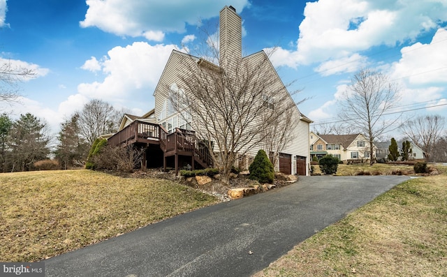 view of property exterior featuring a chimney, aphalt driveway, a yard, an attached garage, and stairs