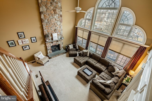 living area with a stone fireplace, a high ceiling, carpet floors, and ceiling fan