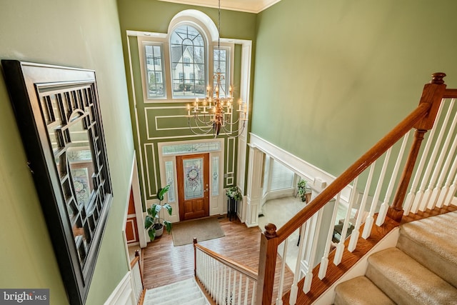 entrance foyer with stairway, a notable chandelier, wood finished floors, and ornamental molding