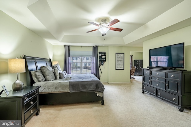 bedroom featuring a raised ceiling, light colored carpet, baseboards, and ceiling fan