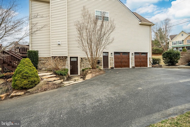 view of side of property with aphalt driveway, stone siding, and an attached garage