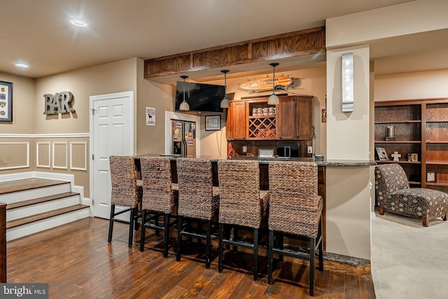 bar with a wainscoted wall, wet bar, dark wood finished floors, pendant lighting, and a decorative wall