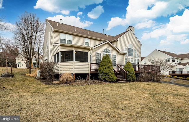 rear view of property with a sunroom, a yard, a shingled roof, a wooden deck, and a chimney