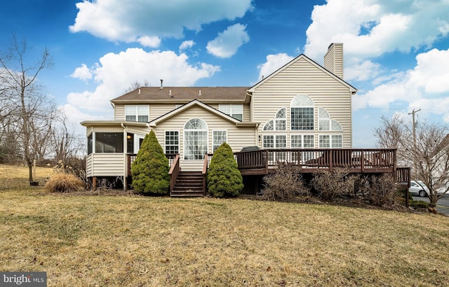 rear view of property featuring a lawn, a deck, a chimney, and a sunroom